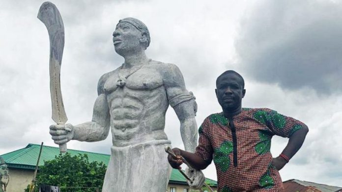 Monday Aigbe standing alongside a statue of his great-grandfather, one of the sculptors of the famous Benin Bronzes